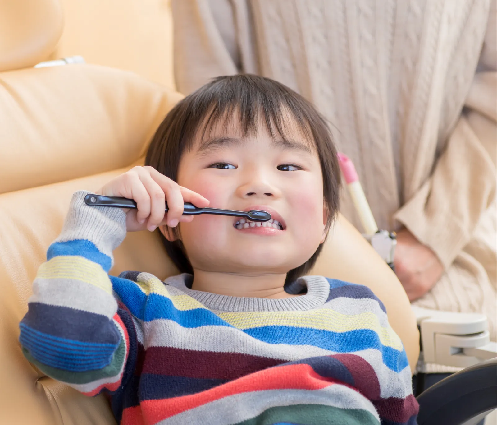 歯ブラシをくわえて診療台に座る男の子の写真